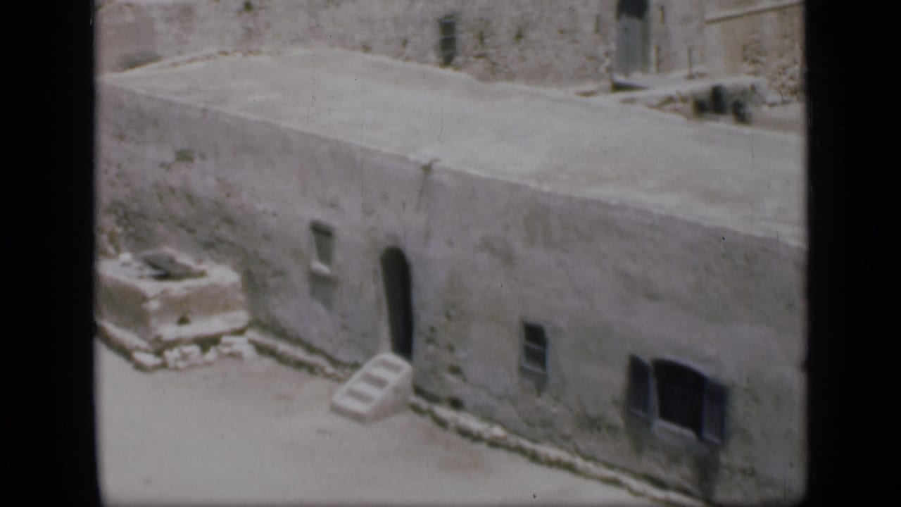 Weathered pale stone building with small windows, steps, and an arched doorway.