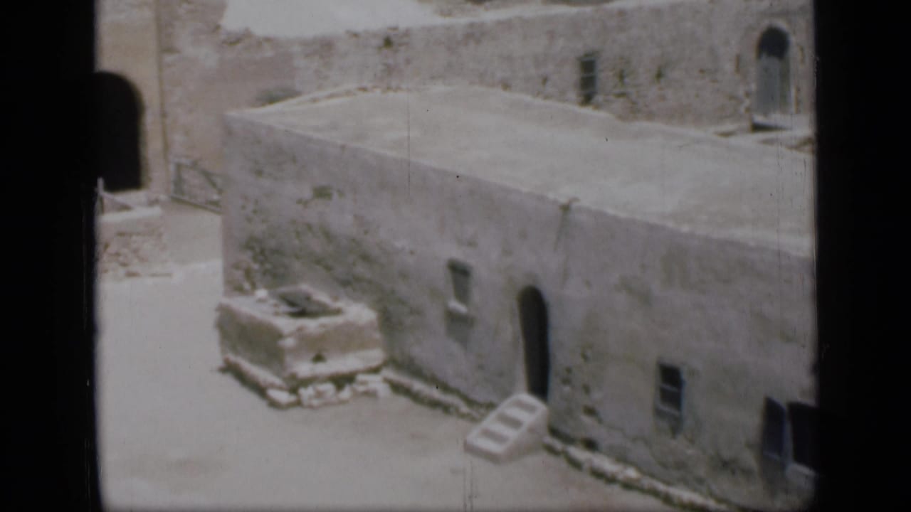 Stone building facade with arched doorway, small window, and steps in bright light.