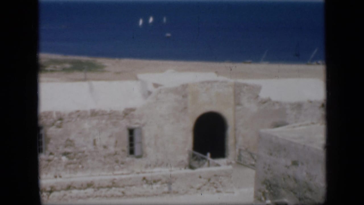1946 Egypt 8mm frame showing weathered stonework, an arched opening, and a blue sea horizon beyond the buildings.