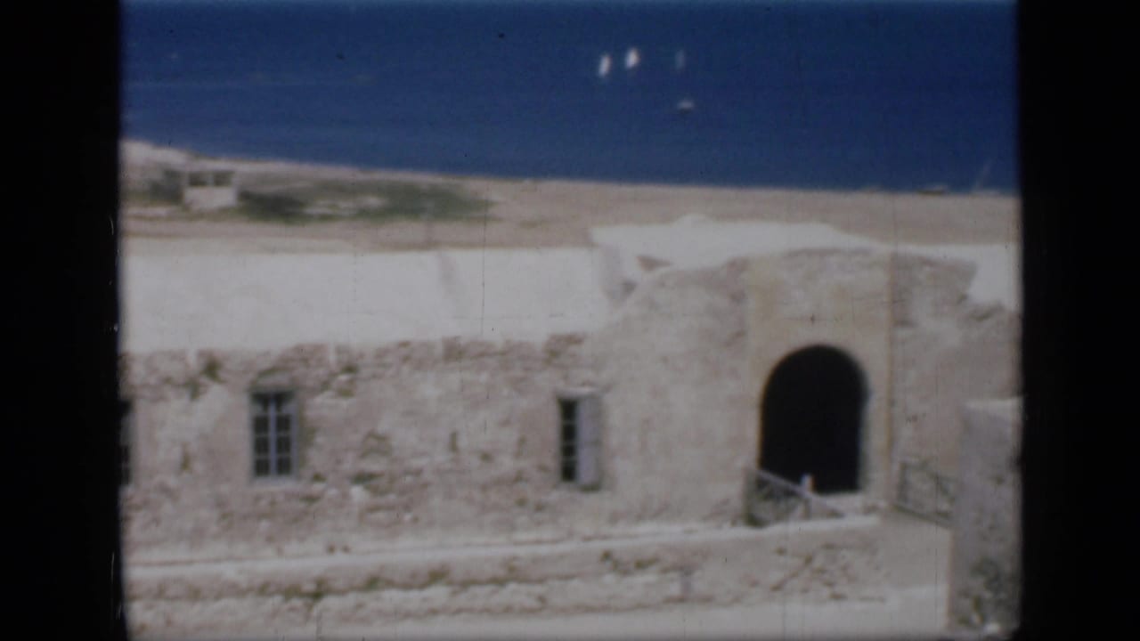 1946 Egypt 8mm frame with stone walls and an arched doorway in front of a blue sea horizon with distant sailboats.