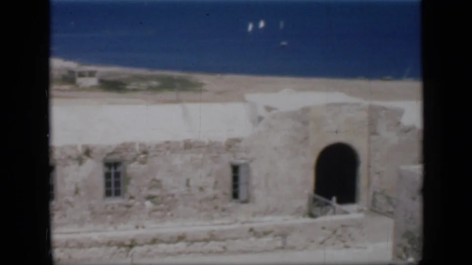 1946 Egypt 8mm frame with stone walls and an arched doorway in front of a blue sea horizon with distant sailboats.