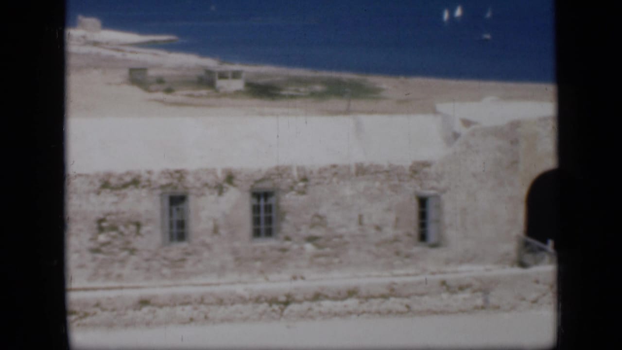 Stone beachside building with barred windows and water beyond.