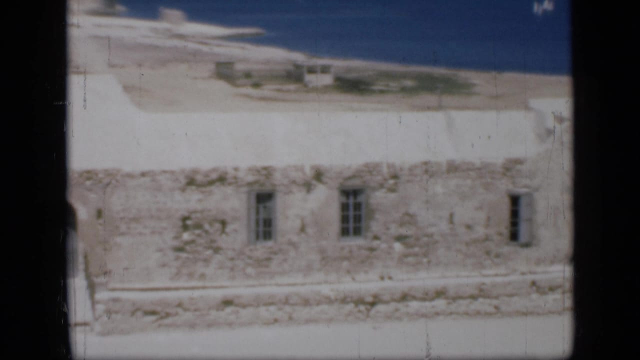 1946 Egypt home-movie view of a whitewashed coastal wall with small barred openings and a blue shoreline in the background.