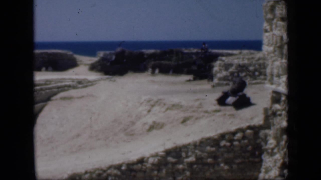 Stone ruins partly buried in sand with blue water on the horizon.