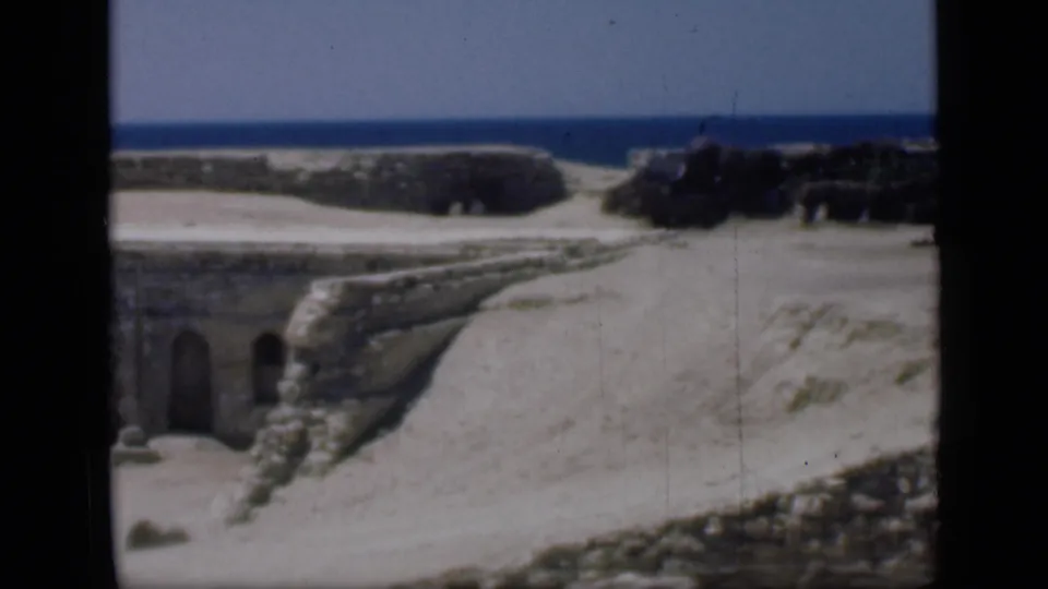 1946 Egypt 8mm frame showing arched stone openings, a sloped sandy ruin wall, and blue water across the background.