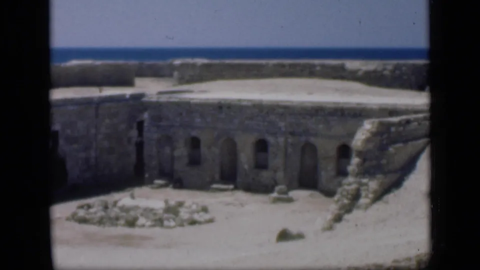 1946 Egypt travel frame showing a closer section of weathered fortification wall, arched doorways, rubble, and sunlit sand.