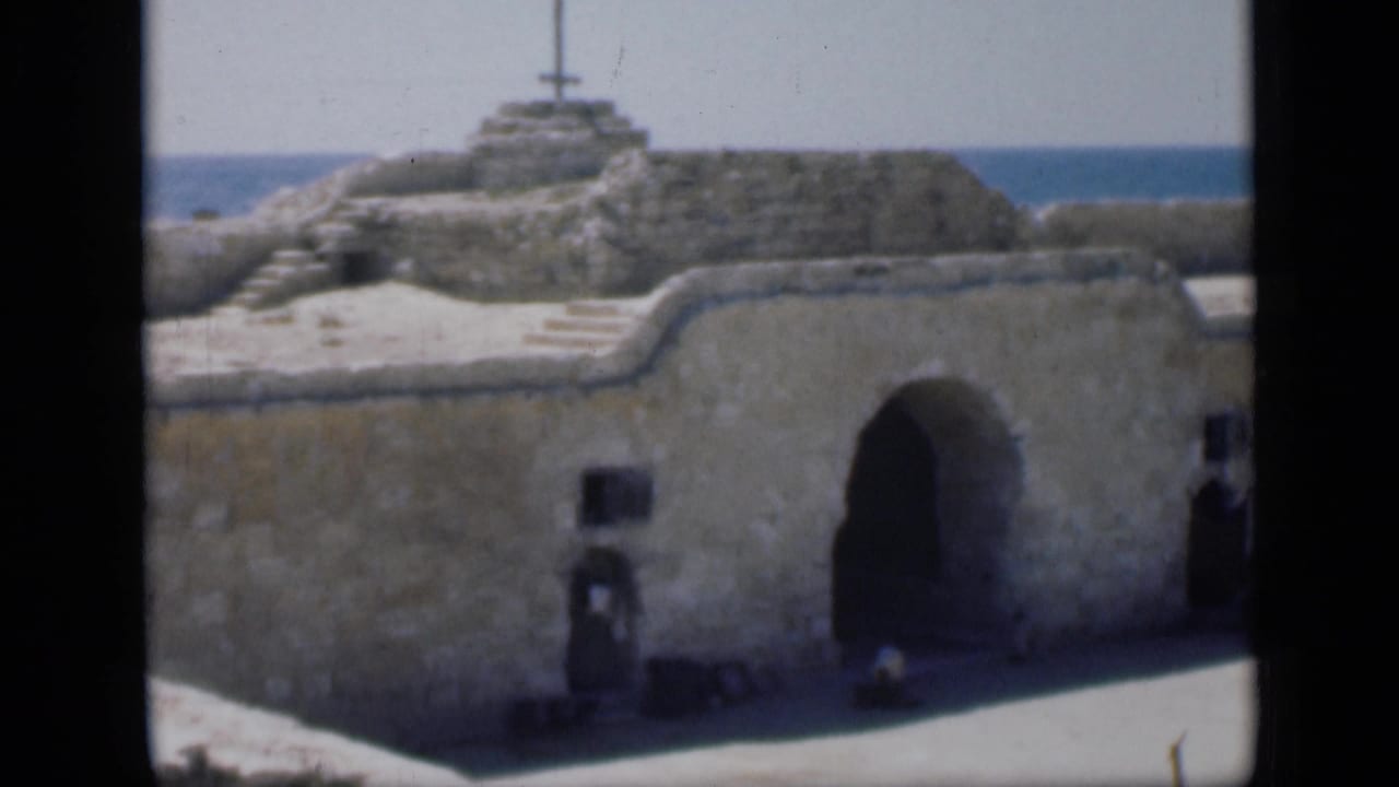 1946 Cairo-labeled 8mm frame showing a weathered religious-looking stone facade with an arched entrance and blue water beyond.