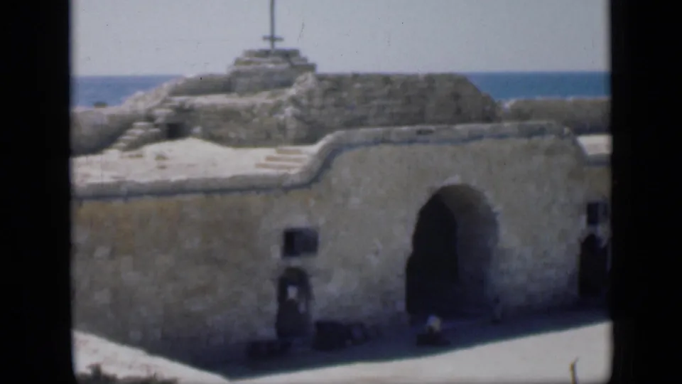 1946 Cairo-labeled 8mm frame showing a weathered religious-looking stone facade with an arched entrance and blue water beyond.
