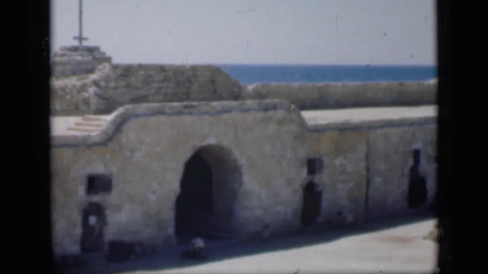 1946 Cairo-labeled 8mm frame holding on a weathered stone wall with an arched entrance and coastal water behind it.