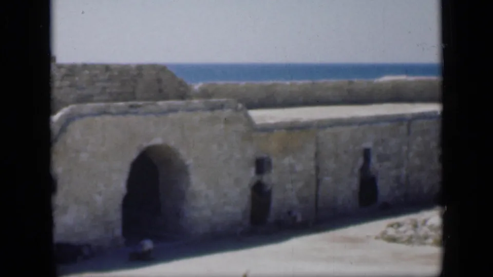 1946 Cairo-labeled home-movie frame showing a weathered religious-looking stone facade, dark openings, and water beyond.