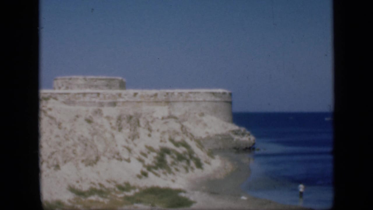 Coastal stone fort on a rocky cliff above a blue sea.