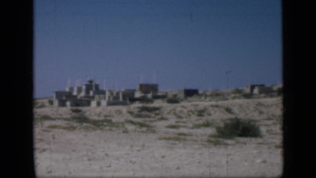 1946 Cairo-area home-movie frame showing sandy ground, sparse scrub, and low stone buildings under blue sky.