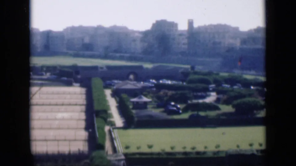 1946 Cairo frame showing a formal garden with a paved approach, manicured lawns, hedges, cars, and pale skyline buildings.