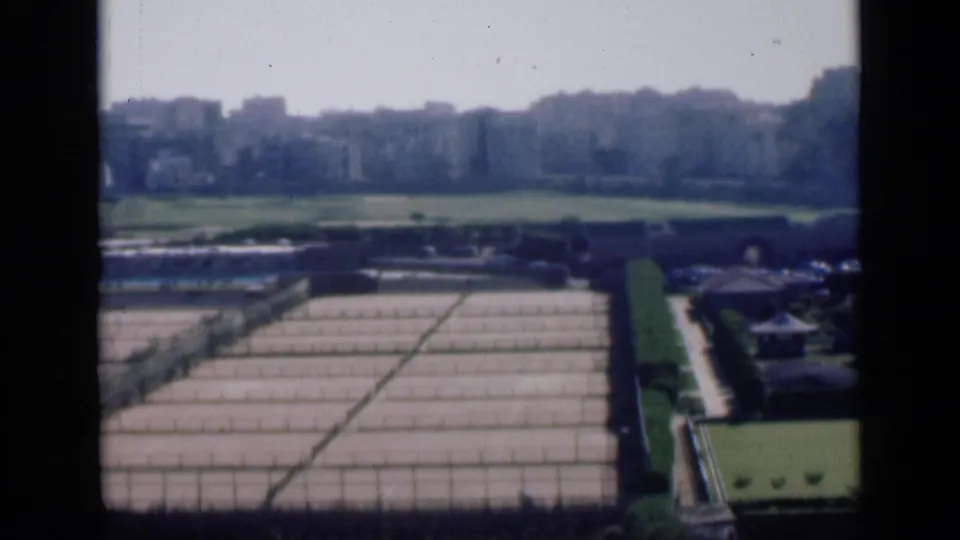 1946 Cairo home-movie frame with cultivated rectangular plots in the foreground and a hazy band of urban buildings beyond open land.