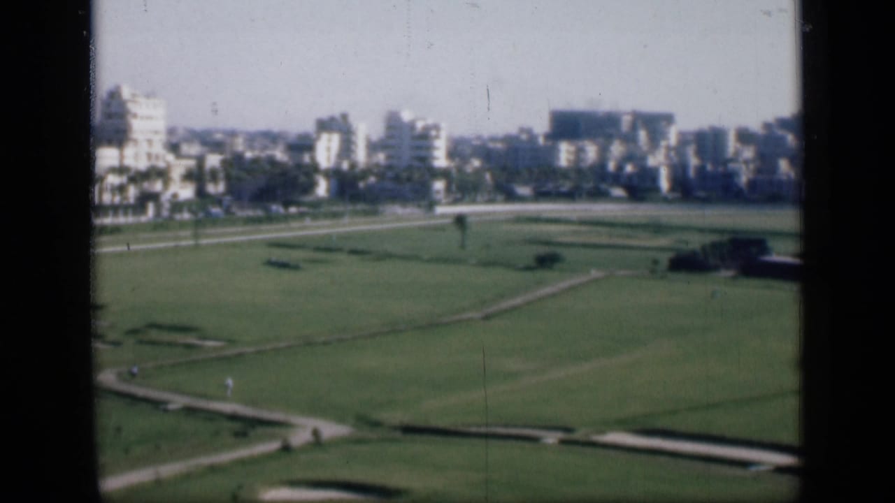 Wide green field with winding paths and a distant skyline behind a dark vertical frame.