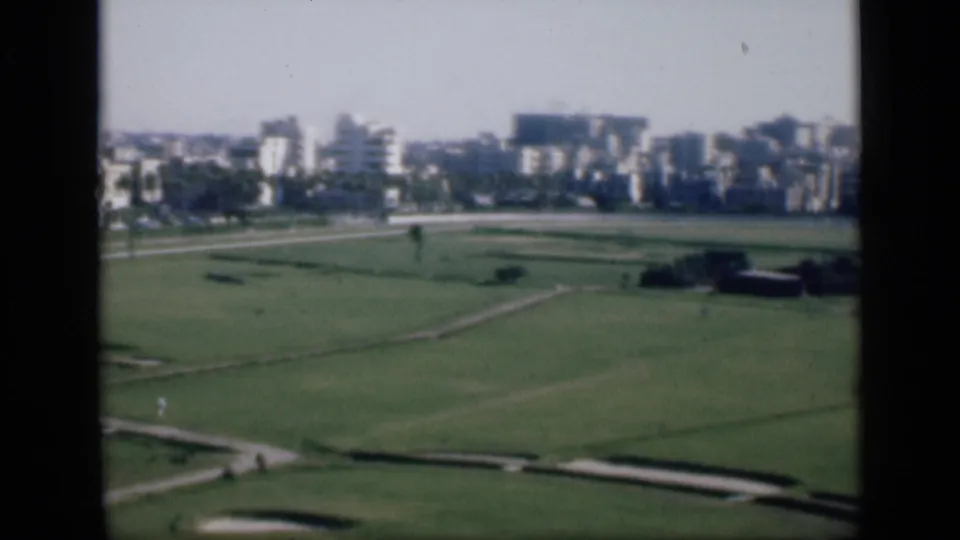 Soft 8mm frame from Cairo in 1946, showing open recreational grounds with paths, sand-trap-like areas, and distant urban buildings.
