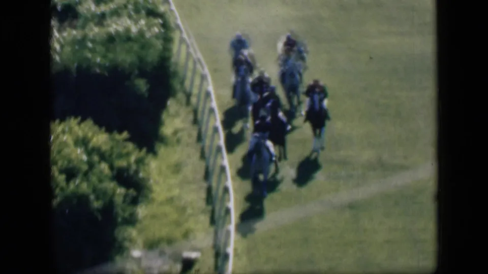 1946 Cairo home-movie frame of the horse race continuing along the bend, with riders spread across the grass track.