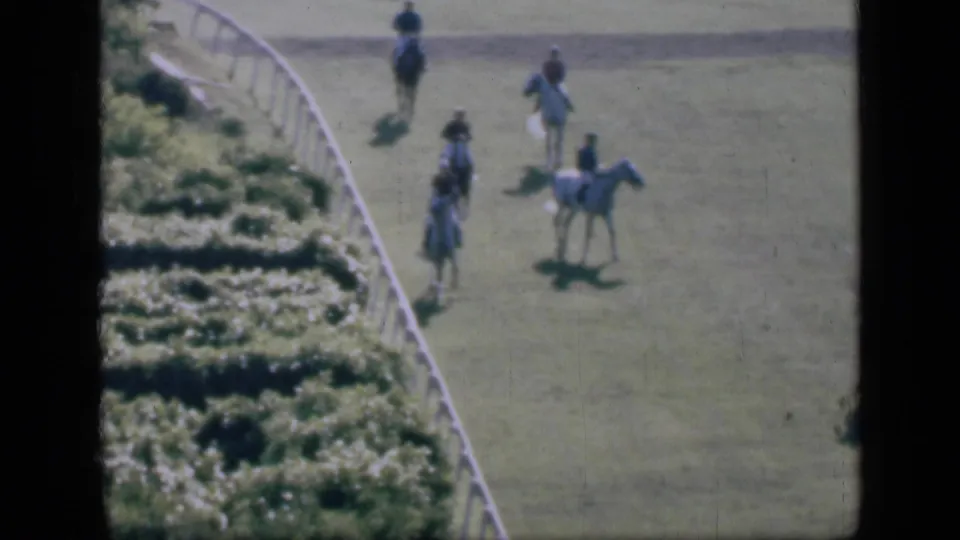Several jockeys on light and dark horses appear on a Cairo racetrack, seen from above in soft 8mm color footage.