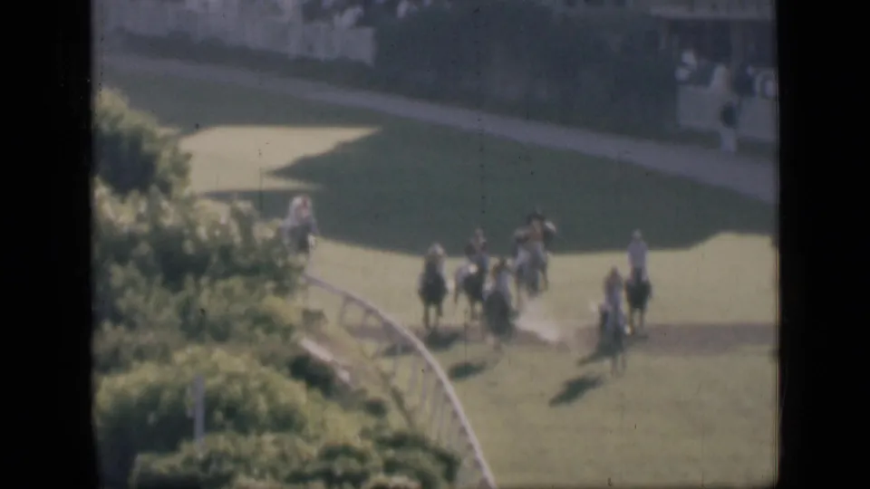 1946 Cairo home-movie frame showing horse riders rounding a green racecourse bend, with spectators in the background.