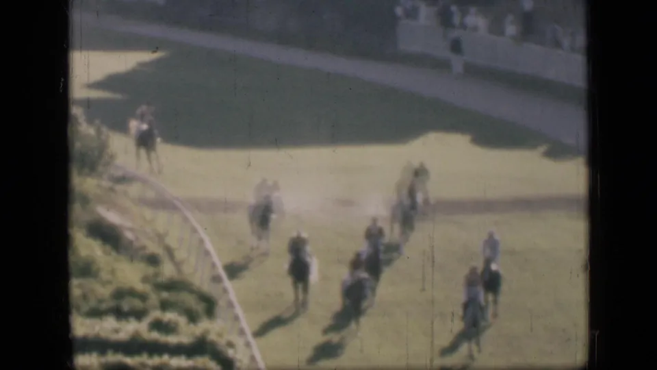 Soft 8mm frame from 1946 Cairo showing jockeys and horses passing a rail-lined curve on a green track.
