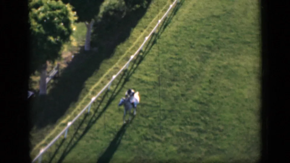 1946 Cairo 8mm frame showing a mounted rider on a light horse near a white rail fence, with long shadows across grass.
