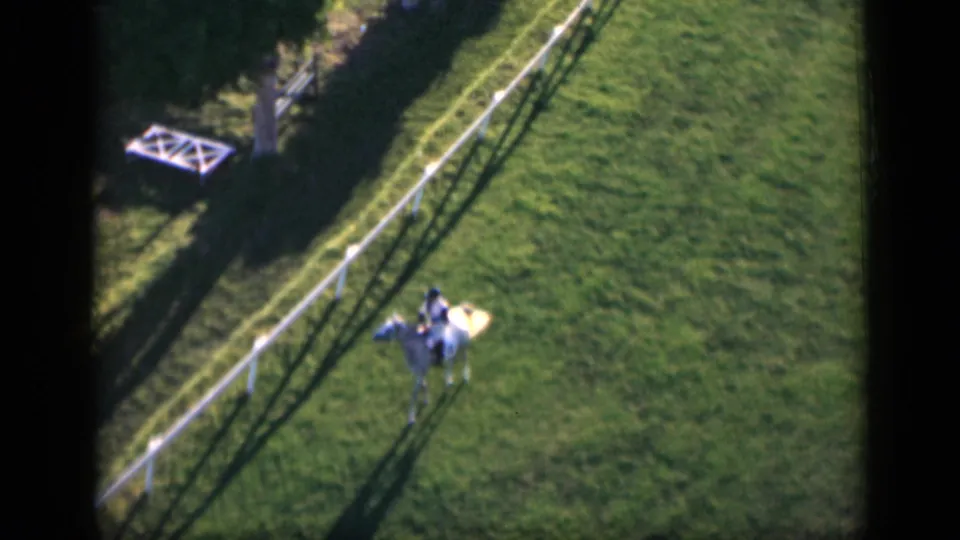 Elevated 1946 Cairo home-movie view of a rider on a light horse passing along a white fence in an open field.