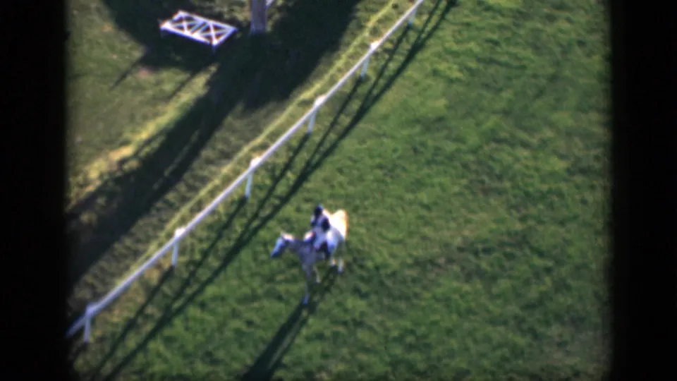 Soft 8mm frame from Cairo in 1946 showing a rider on a pale horse crossing the field near a white fence.