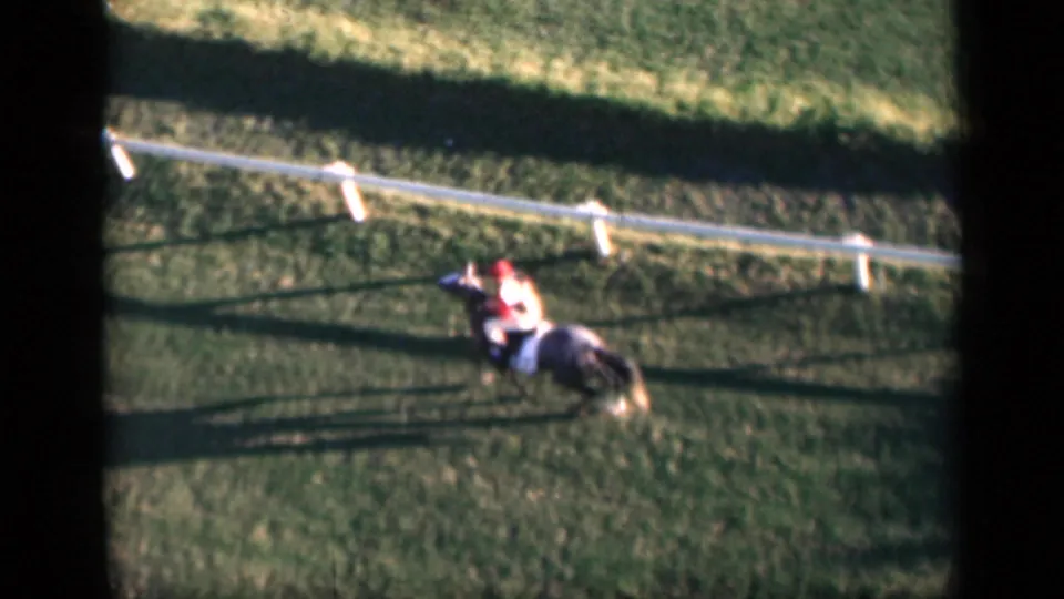 1946 Cairo frame showing a rider on horseback moving beside a white fence, with strong late-day shadows across the grass.