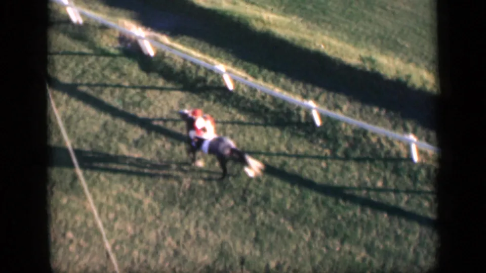 High-angle 1946 Cairo frame showing a jockey on a dark racehorse warming up on a fenced grass track.