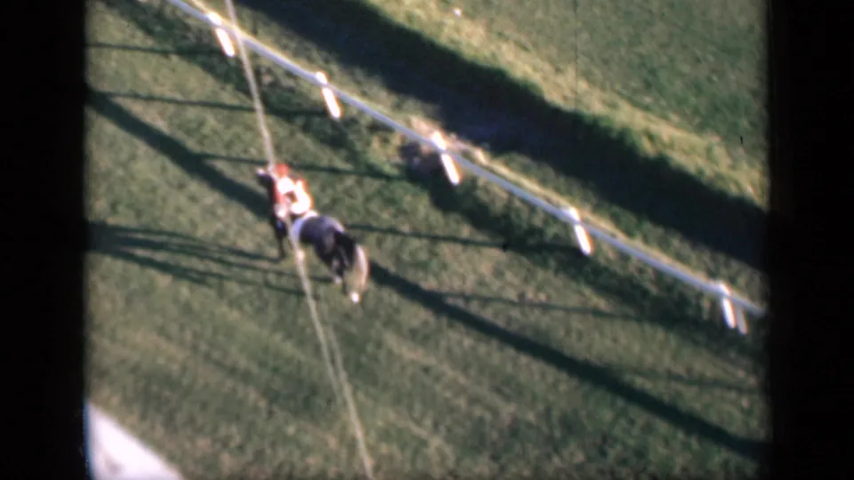 1946 Cairo home-movie still with the horse and jockey seen from above on a grassy racecourse with rail fencing.