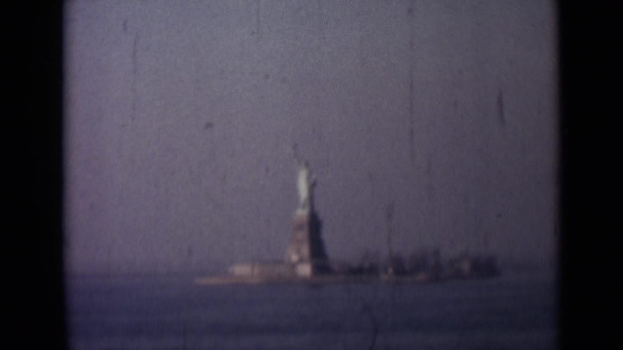 1940s 8mm frame showing a distant Statue of Liberty view across water, with soft focus, scratches, and visible film gate borders.