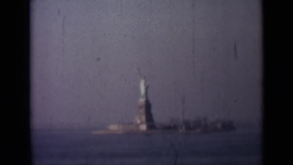 1940s 8mm frame showing a distant Statue of Liberty view across water, with soft focus, scratches, and visible film gate borders.