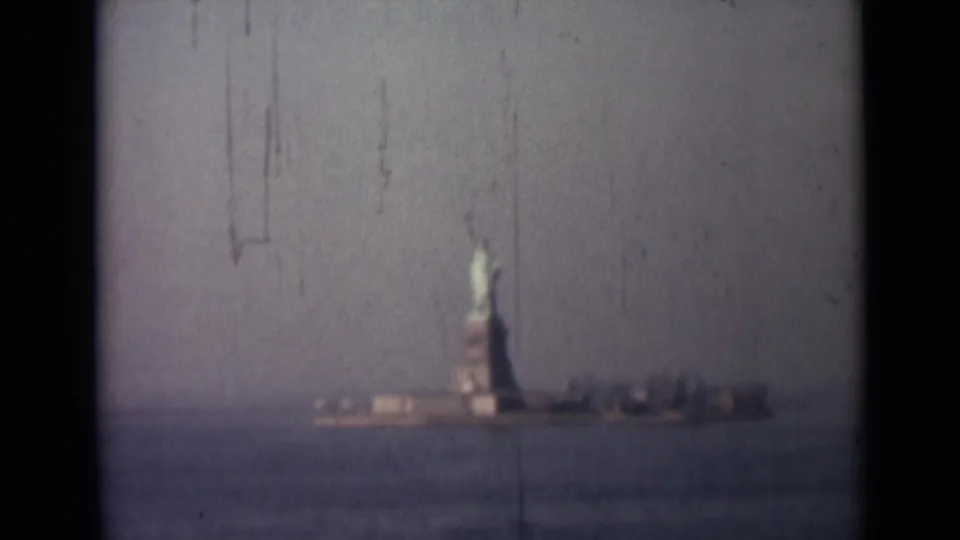 End frame of a 1940s 8mm landmark view, showing the Statue of Liberty across water with shoreline structures and film wear.