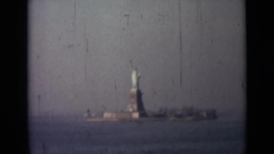 1940s 8mm view of the Statue of Liberty from across New York Harbor, framed by dark gate edges and visible film wear.