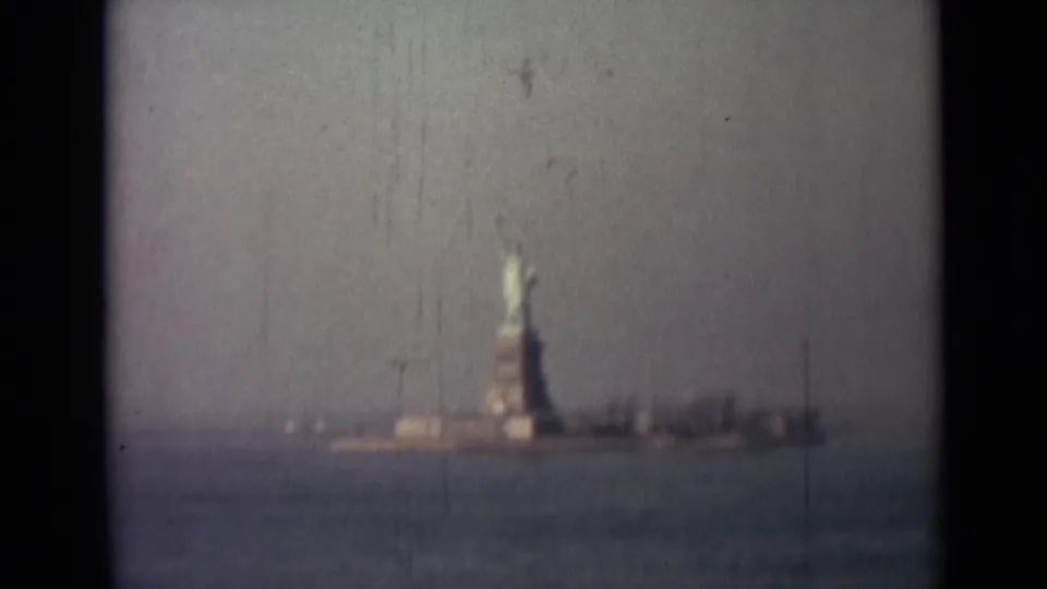 1940s 8mm frame showing the Statue of Liberty from across the water, softened by haze, grain, and motion blur.