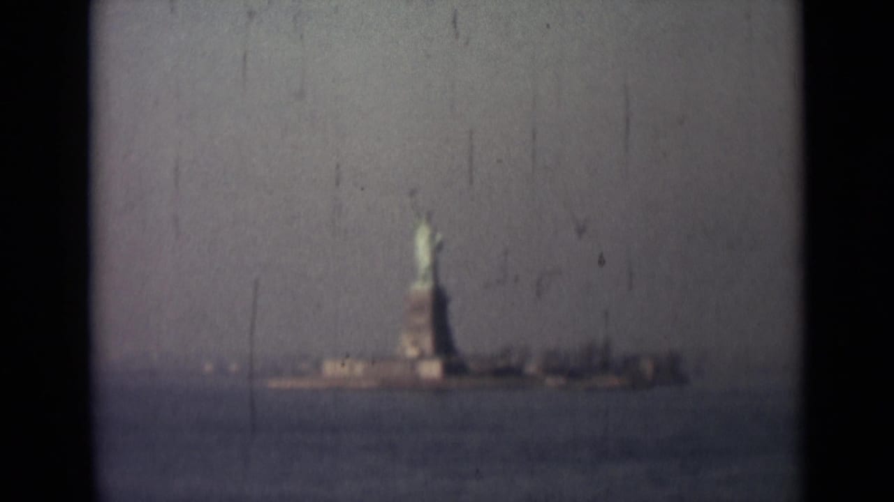 Distant Statue of Liberty across harbor water with dark film borders and soft focus.