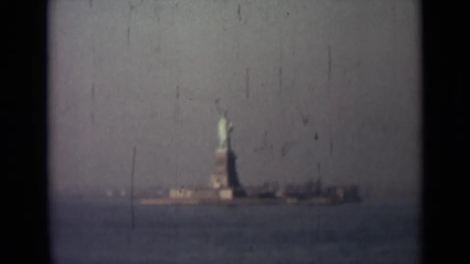 1940s 8mm frame appearing to show the Statue of Liberty from across the water, with hazy sky, muted color, and visible film wear.
