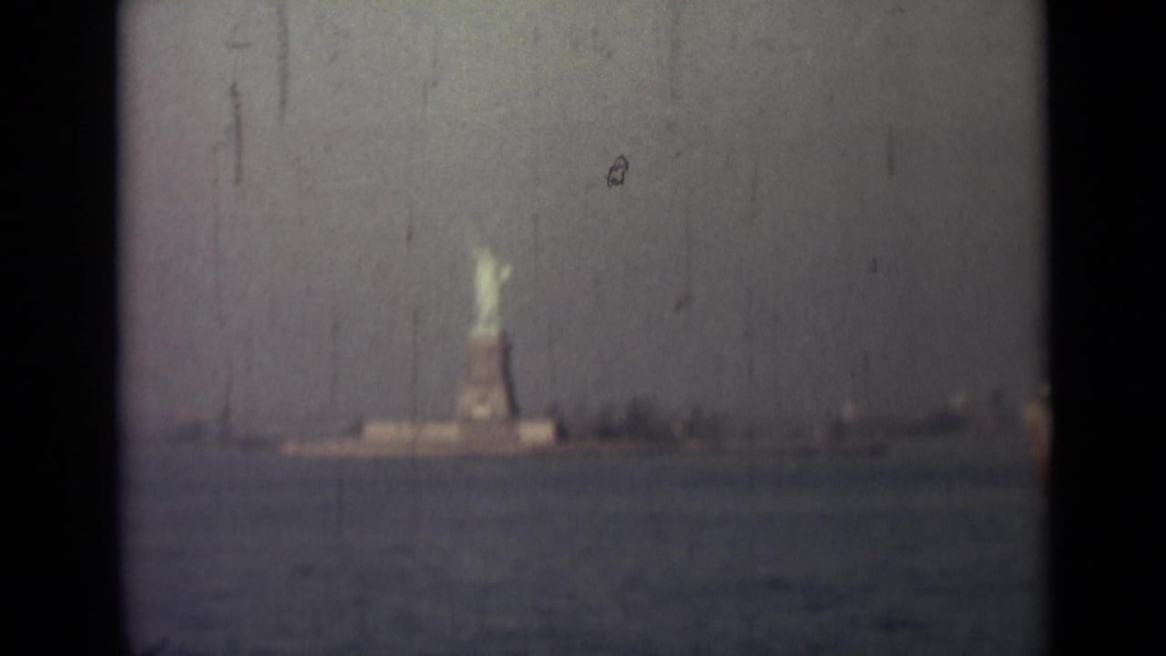 Statue of Liberty centered at a distance across water under a hazy sky.
