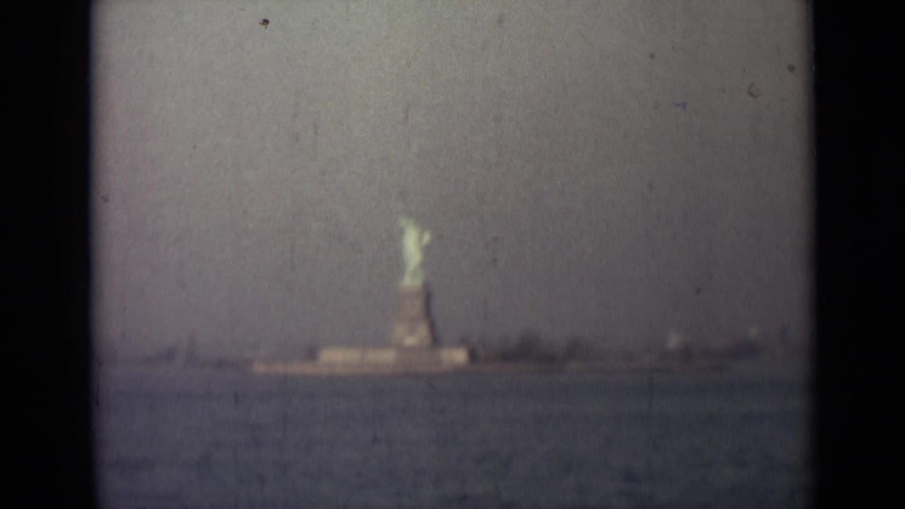Distant Statue of Liberty across harbor water in a soft, scratched film frame.