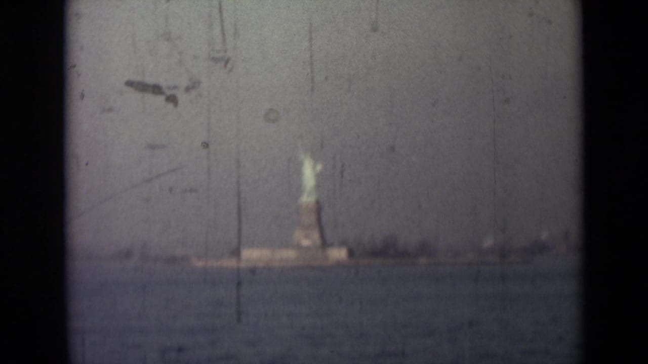 Distant Statue of Liberty centered beyond water with dark film borders and scratches.