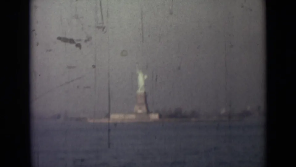 The Statue of Liberty remains distant across harbor water, framed by dark 8mm gate edges and a muted, scratched sky.