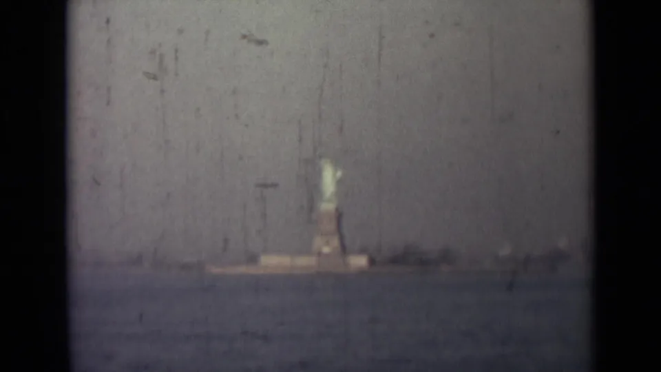 The statue and pedestal are slightly larger in frame, still viewed from across the harbor with soft focus and surface scratches.