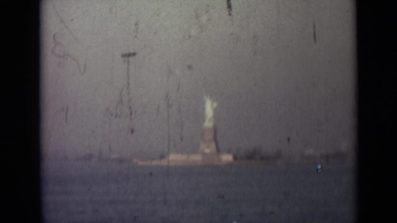 Distant Statue of Liberty seen across water through a faded film frame.