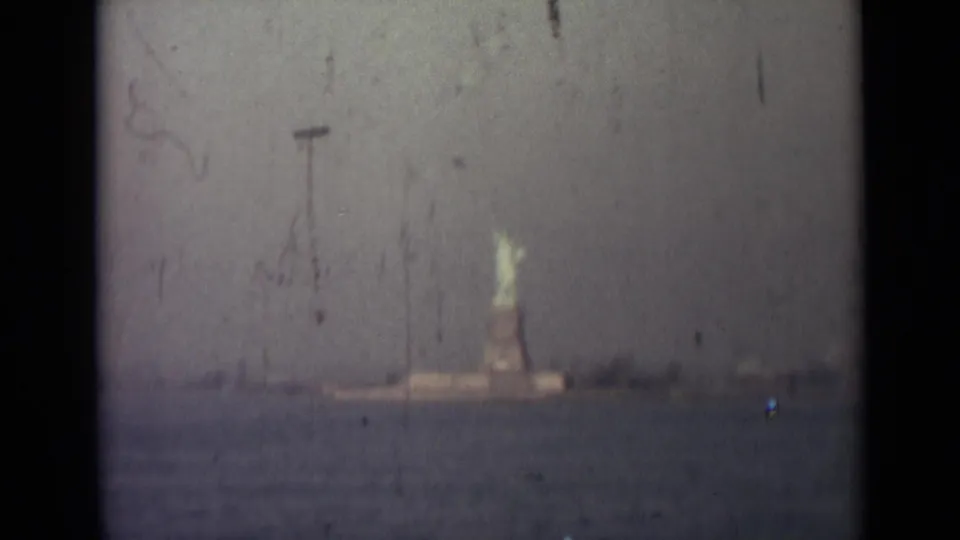 Distant Statue of Liberty across a hazy harbor, seen in faded 8mm home-movie footage from the 1940s travel sequence.