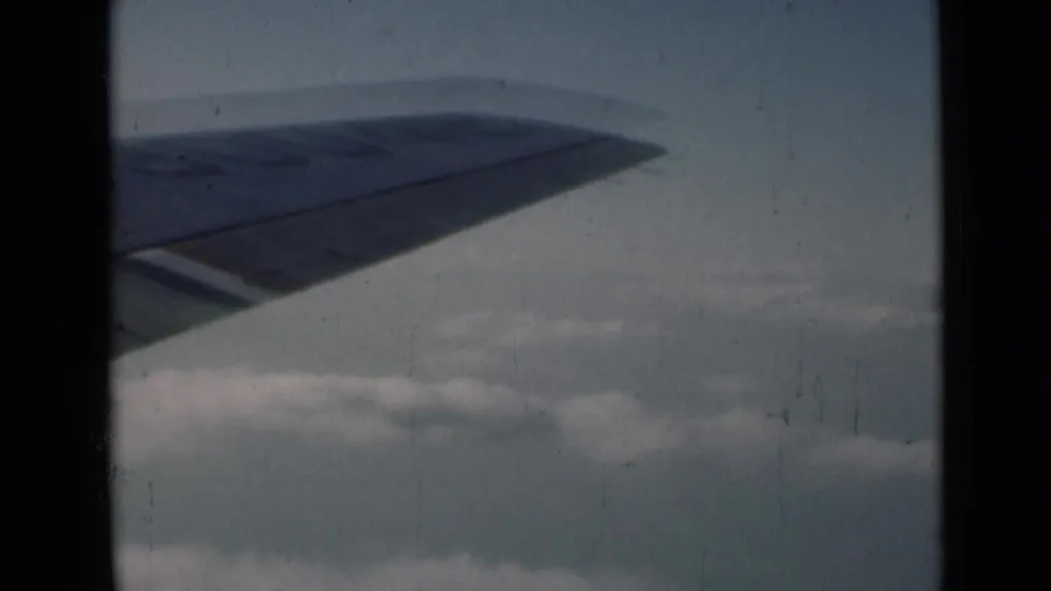 Final 1946 London-context frame with airplane wingtip, pale sky, cloud layers, and visible 8mm film grain.