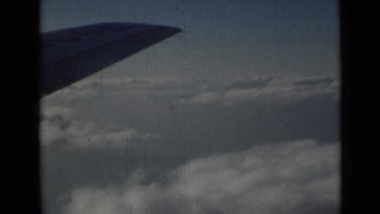 Airplane wing silhouette above layered clouds and pale sky.