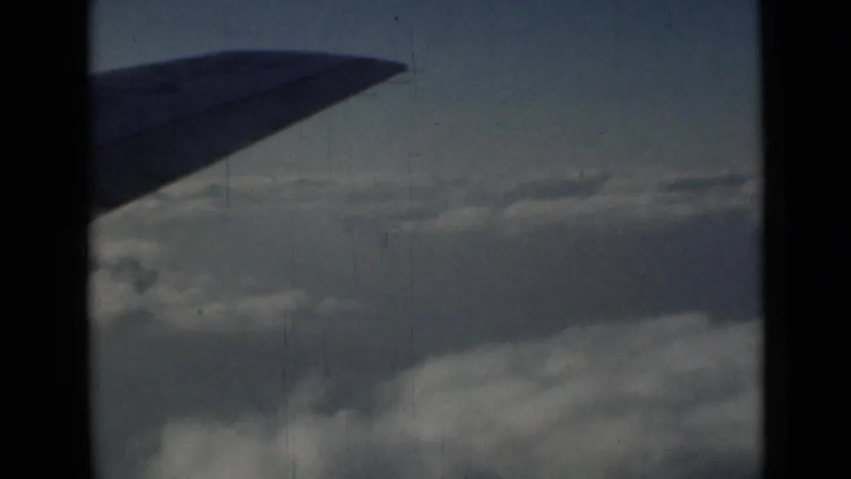1946 8mm airplane-window view near London metadata, with a dark wing cutting across a soft cloudscape.