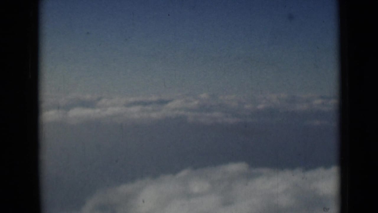 Aerial sky view from the 1946 London-attributed 8mm clip, with pale cloud banks and dark scan borders.