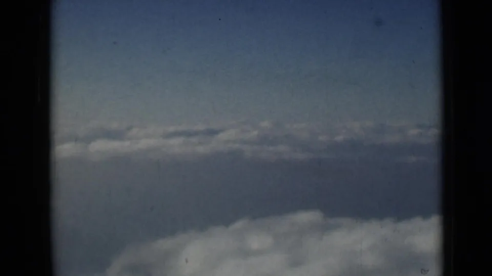 Aerial sky view from the 1946 London-attributed 8mm clip, with pale cloud banks and dark scan borders.