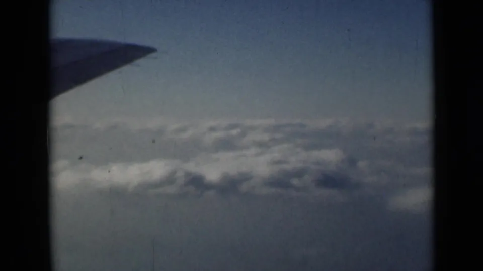 1946 home-movie frame showing an airplane wing over white and gray clouds in pale blue sky, based on supplied London travel metadata.
